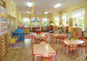 przestronna sala grupy piątej ze stolikami i krzesełkami dla dzieci oraz dekoracjami zawieszonymi pod sufitem